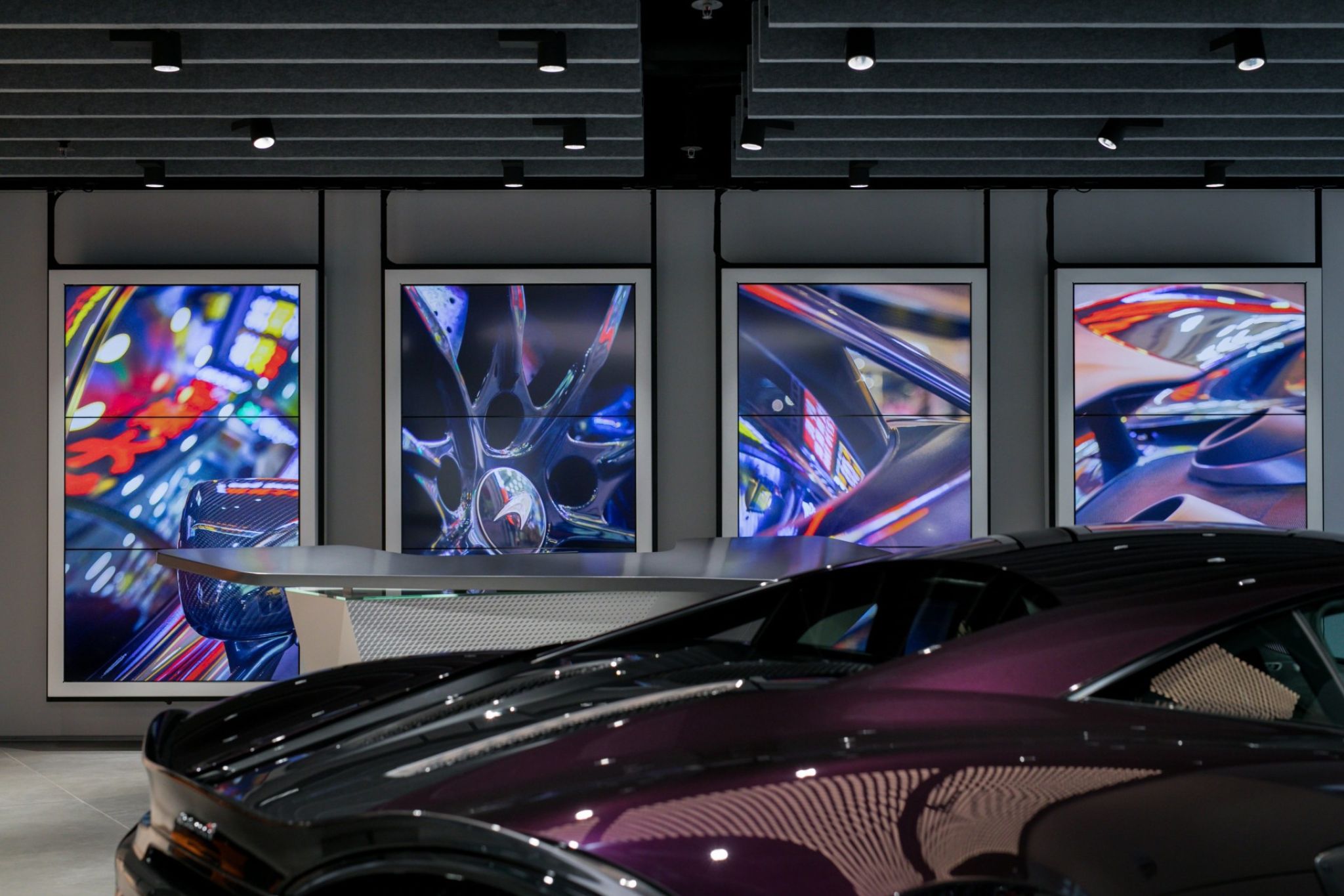 Interior of a retail space of the car manufacturer McLaren with a sports car in the foreground and displays hanging from the ceiling.
