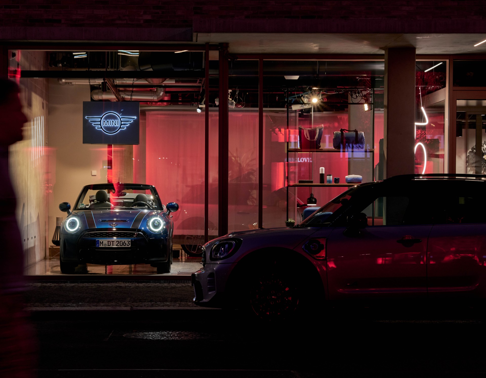Red illuminated shop window of a building with cars of vehicle manufacturer MINI displayed inside.