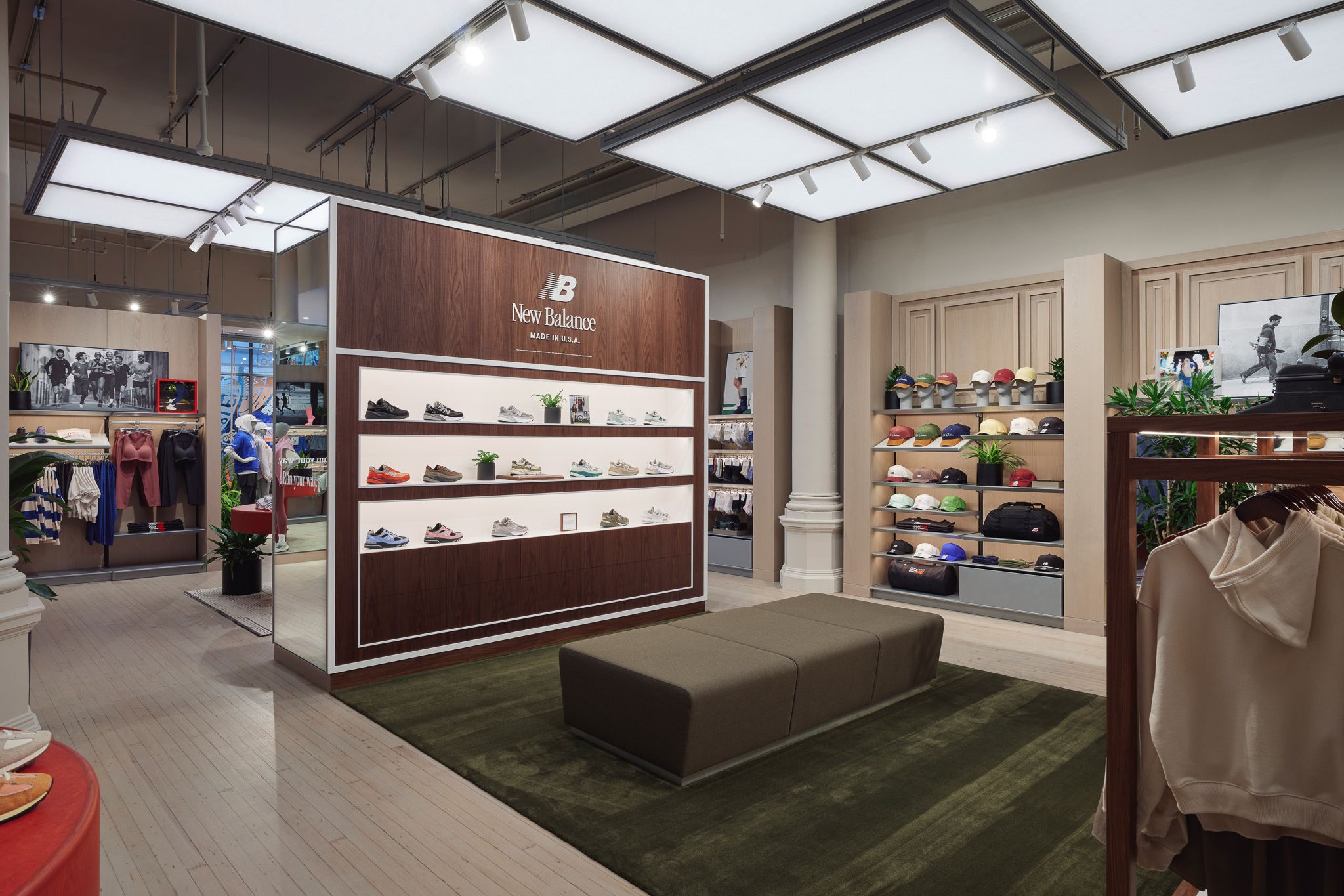 Interior of a New Balance store featuring illuminated wall shelves with shoes, clothing racks, and a bench on a green rug.